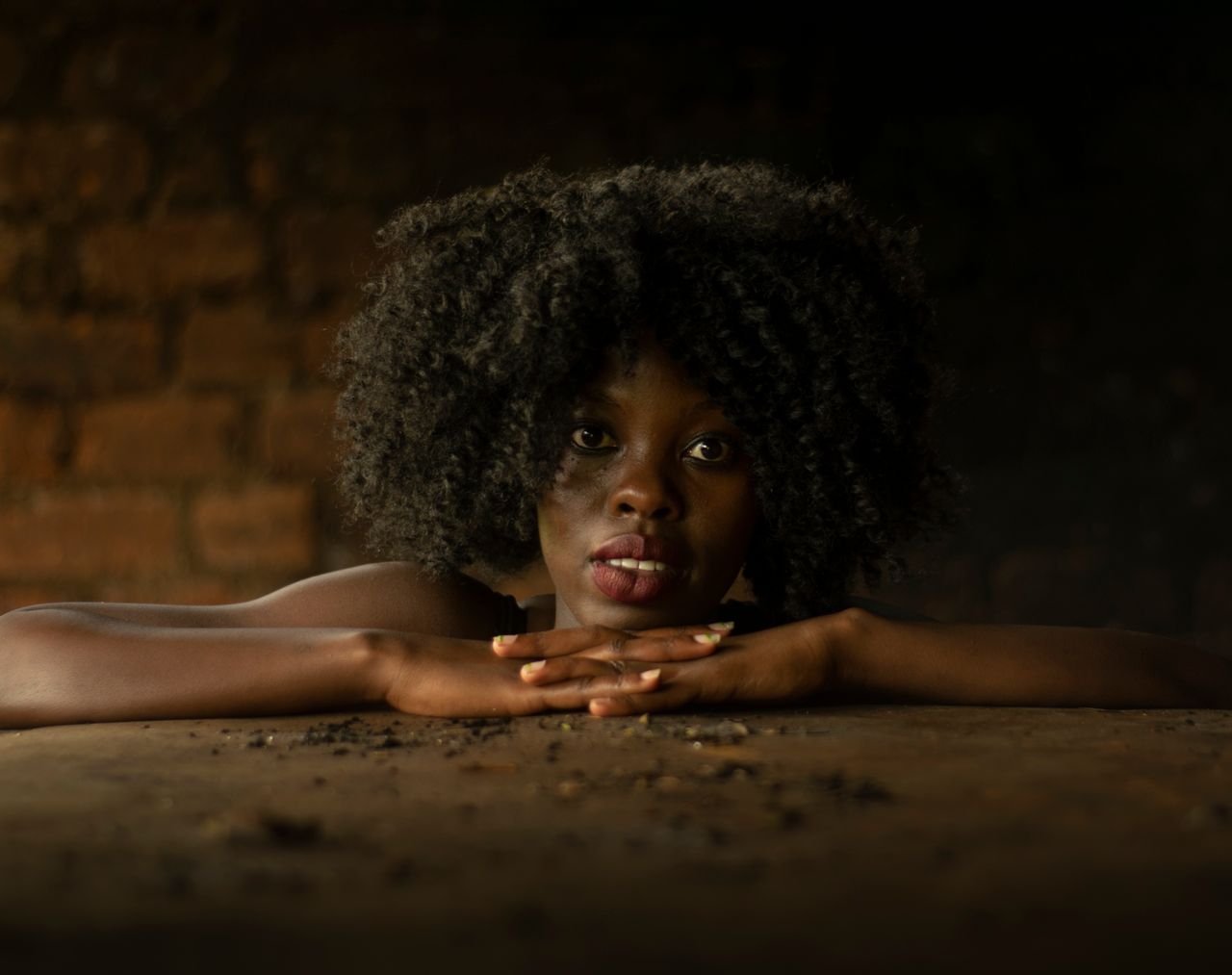 Striking portrait of a woman with afro hair leaning on a rustic surface in Kenya.