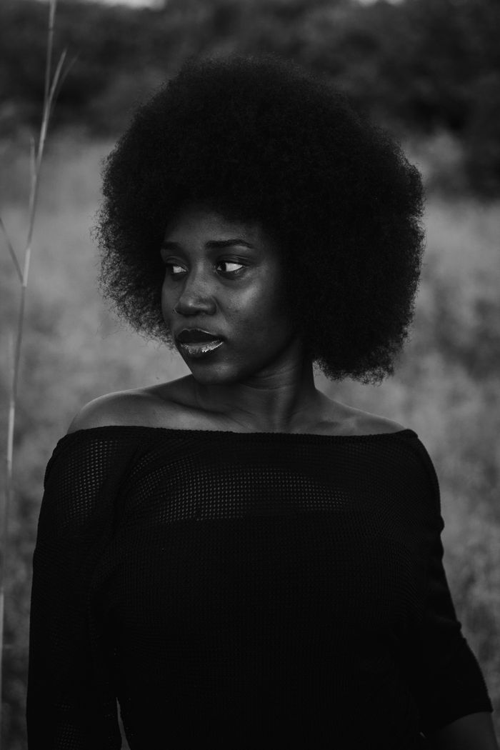 Artistic black and white portrait of a woman with afro hair in a natural setting.
