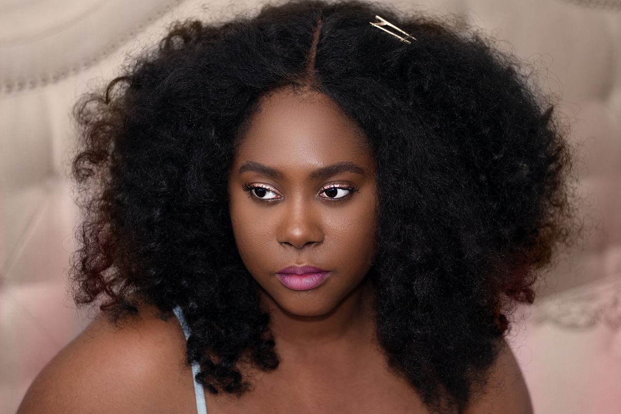 Close-up portrait of a woman with natural curly hair and pink lipstick, showcasing beauty.
