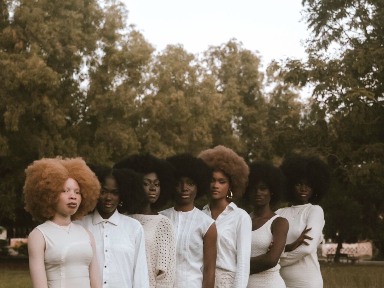 Group of women with stylish afro hairstyles posing elegantly outdoors against a backdrop of lush greenery.
