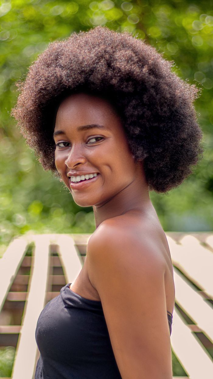 Vibrant portrait of a smiling young woman with afro hair enjoying a sunny day outdoors.