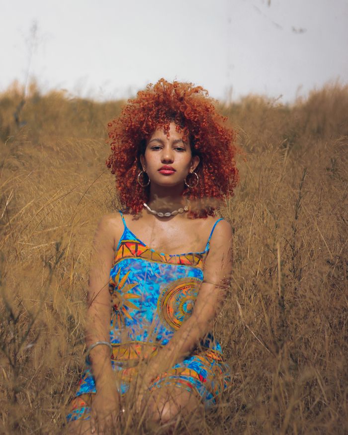 Portrait of a red-haired woman in vibrant dress sitting in a field, Morocco.